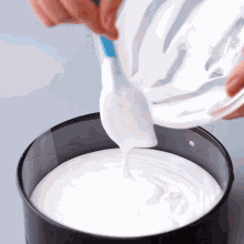 a person is pouring white frosting into a cake pan