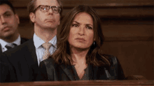 a woman sitting in a courtroom with her eyes closed and a man in a suit behind her