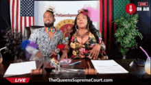 a man and woman are sitting at a desk in front of a sign that says the queens supreme court