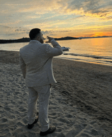 a man in a suit is standing on a beach drinking from a bottle