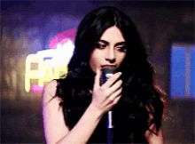 a woman singing into a microphone in front of a neon sign that says a