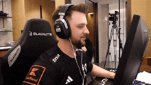 a man wearing headphones and a blacklyte chair looks at a computer screen