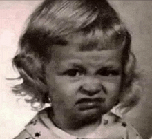 a black and white photo of a little girl with a very angry face .