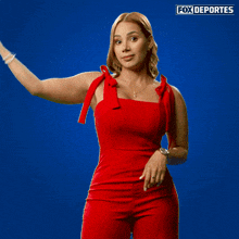 a woman in a red jumpsuit is holding up a fox deportes sign