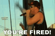 a man singing into a microphone with the words " you 're fired " written below him