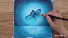 a person is painting a blue butterfly with a brush on a piece of paper that says made in animatica