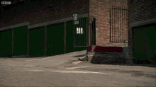 a row of green garage doors next to a brick wall with bbc written on the bottom