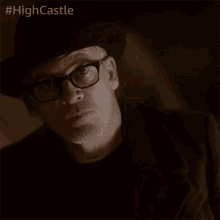 a man wearing glasses and a hat with the hashtag #highcastle on the bottom