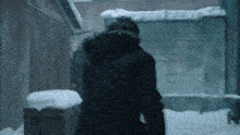 a man in a black jacket is walking through the snow in a dark alleyway .