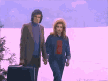a man and a woman are walking in the snow with a suitcase