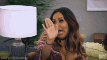 a woman is waving her hand in front of a lamp while sitting on a couch .