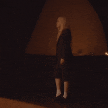 a woman in a black suit and white socks is standing in a dark room