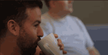 a man with a beard drinking from a white coffee mug