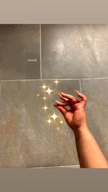 a woman 's hand with long nails is reaching up towards a tile wall with the words mood written on it