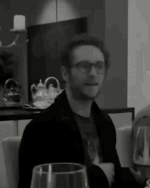 a man wearing glasses sits at a table with a glass of wine in front of him