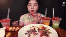 a woman eating a slice of watermelon next to a plate of fruit salad