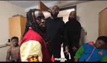 a group of men are standing in a room and one of them has a red jacket on