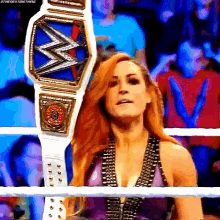a woman is standing in a wrestling ring holding a wrestling belt .