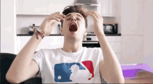 a young man wearing a white t-shirt with a mlb logo on it yawning