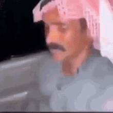 a man with a mustache is wearing a pink head scarf and looking at the camera .