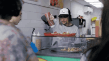 a man wearing a white hat with the letter l on it pours ketchup on a tray of food