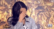 a woman is covering her face with her hand while standing in front of a gold background .