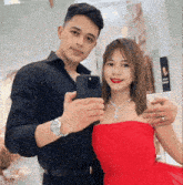 a man in a black shirt is taking a picture of himself and a woman in a red dress .