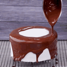 chocolate is being poured on a cake that is on a cooling rack
