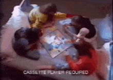 a group of children are playing a board game on a bed with the words cassette player required above them .