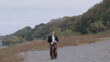 a man in a suit and floral pants stands in a field