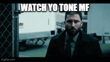 a man in a suit and tie is standing in front of a chain link fence with the caption watch yo tone mf