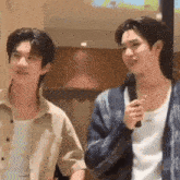 two young men are standing next to each other in a room . one of the men is holding a microphone .