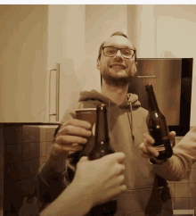 a man with glasses is holding two bottles of beer and a cup