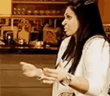 a woman in a white shirt is standing in a kitchen holding something in her hands .