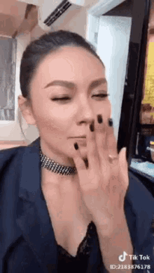 a woman with black nails and a choker is applying makeup on her face .