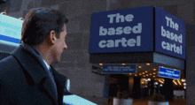 a man in a suit and tie stands in front of a sign that says the based cartel