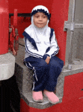 a little girl wearing a hijab sits on the steps of a red truck