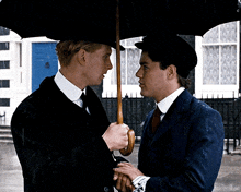 a man in a suit holds an umbrella over another man