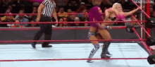 two women are wrestling in a wrestling ring with a referee standing behind them .