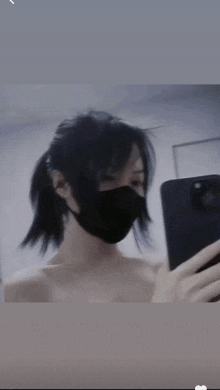 a woman wearing a black mask takes a selfie with her phone