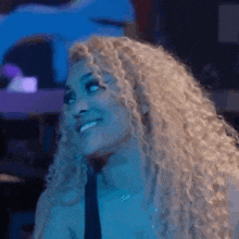a woman with curly blonde hair is smiling in a dark room with blue lights .