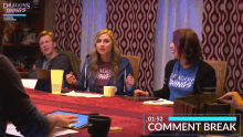 a group of people sitting around a table wearing dragons things t-shirts