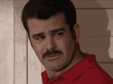 a man with a mustache and a red shirt looks sad