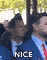 a man in a suit and tie says nice in front of a crowd