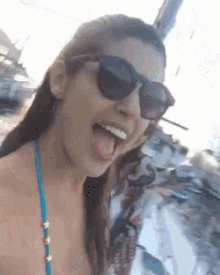 a woman wearing sunglasses and a blue bikini is making a funny face .