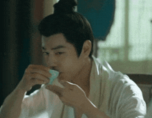 a man in a white robe is drinking from a cup .