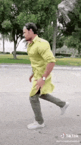 a man in a yellow shirt and khaki pants is walking down a street .