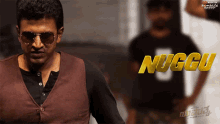 a man wearing sunglasses stands in front of a poster that says nuggu