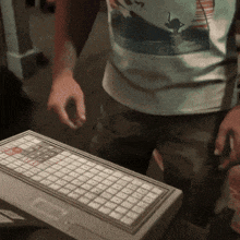 a man wearing a shirt with a swan on it is standing next to a keyboard