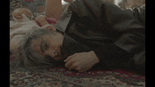 a woman in a black leather jacket is laying on a rug